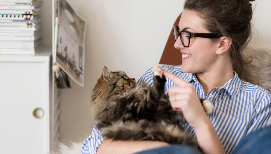 Uma mulher sentada com o seu gato no colo a tocar com o seu dedo na pata dele