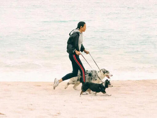 mulher a correr na praia com os seus cães